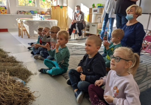Dzieci siedzą na dywanie i oglądają przedstawienie. Są skupione.