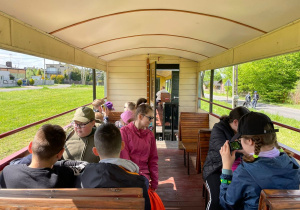 Uczniowie siedzą na ławkach wagoników kolejki.