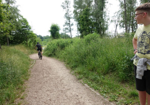 Uczeń obserwuje rowerzystę na ścieżce w lesie.