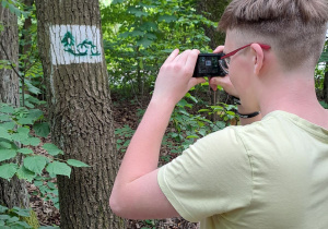 Uczeń fotografuje znak graficzny namalowany na drzewie.
