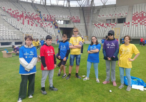 Dziewczęta i chłopcy, ubrani w kolorowe koszulki organizatorów, na murawie stadionu.