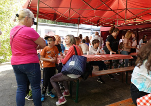 Uczestnicy pikniki siedzą przy długich stołach.