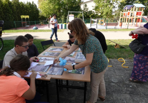 Uczniowie siedzą wokół stołu, na którym rozłożone są zdjęcia bajkowych pomników.