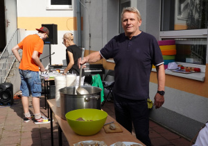 Wychowawca trzyma chochlę, która nalewa zalewajkę z blaszanego kotła.