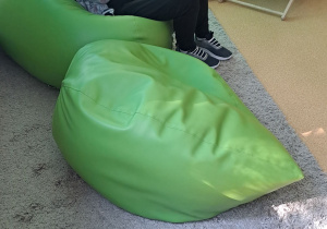 Chłopiec siedzi na miękkiej pufie, w ręku trzyma pluszową pandę. W tle leżaki.