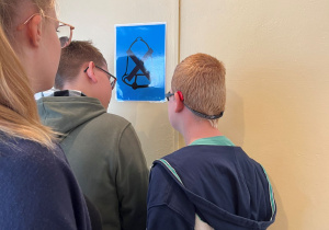 Uczniowie stoją przed ścianą, na której wisi piktogram z przekreślonym dzwonkiem.