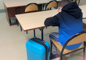 Uczeń siedzący w ławce, obok walizka.