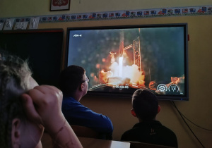 Uczniowie przed monitorem obserwują transmisję ze startu.