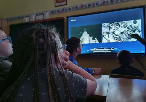 Uczniowie przed monitorem obserwują transmisję ze startu.