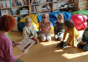 Dzieci siedzą na podłodze. Słuchają nauczycielkę czytającą książkę o kulturze Japonii.