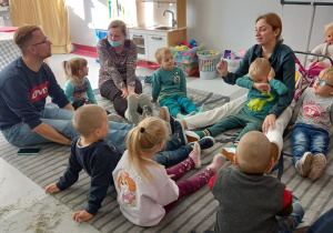 Dzieci siedzą na dywanie i oglądają przedstawienie. Są zaciekawione.