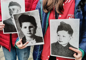 Uczniowie trzymający w rękach czarno-białe zdjęcia dzieci z czasów wojny.