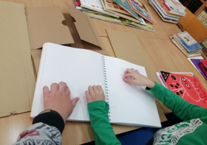 Dzieci oglądają książkę brajlowską, ich dłonie leżą na druku wypukłym.