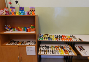 Widok ogólny wystawy: origami i miniatury mumii ułożone na półkach regału i na ławce.