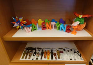 Fragment wystawy: na górze: origami - napis Walentynki i serca; na dole: miniatury mumii wykonane z kolorowej plasteliny z zaznaczonymi szczegółowymi detalami.