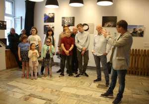 Uczniowie i nauczyciele wraz z twórcami projektu, w tle zdjęcia z wystawy.
