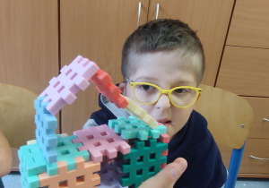 Chłopiec pokazuje zbudowany z klocków domek.