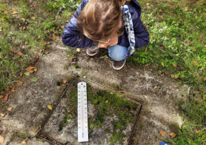 Termometr leżący na ziemi i dziewczynka odczytująca temperaturę gleby.
