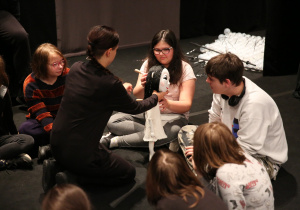 Uczniowie siedzący na podłodze. Dziewczynka dotykająca lalkę.