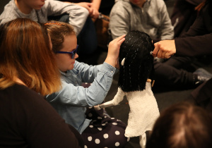 Uczniowie siedzący na podłodze. Dziewczynka dotykająca lalkę.