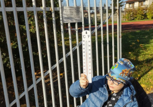 Chłopiec nagrzewa termometr w słońcu.