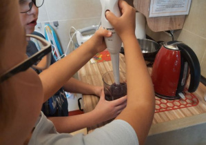 Dziewczynka i chłopiec używają blendera do zrobienia koktajlu.