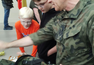 Uczniowie oglądają wyposażenie plecaka wojskowego.
