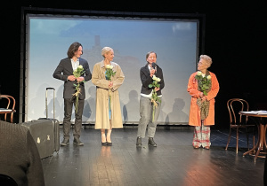 Aktorzy i reżyserka spektaklu z różami w dłoniach stoją na scenie.