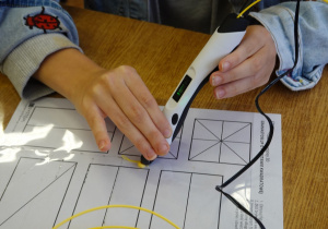 Dziewczynka rysuje długopisem 3D po śladzie - figury geometryczne.