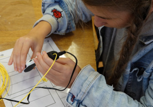 Dziewczynka rysuje długopisem 3D po śladzie - figury geometryczne.