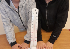 Uczniowie z termometrem, który wskazuje 24 stopnie Celsjusza - pomiar w sali lekcyjnej.