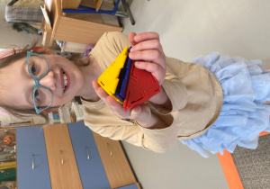 Dziewczynka pokazuje figurę przestrzenną zbudowaną z klocków w kształcie trójkątów..