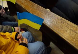 Uczniowie siedzący w ławkach kościoła, w ręku flaga Ukrainy.