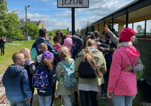 Uczniowie stoją przy wagonikach kolejki, na znaku napis "Jeżów".