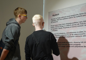 Chłopcy czytają tekst "Wydech" zamieszczony na ścianie.