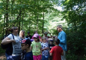 Dzieci słuchające przewodnika podczas zwiedzania lasu.