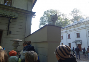 Uczniowie stoją przed budynkiem, na murku pomnik kota.