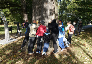 Uczniowie przytulają się do pnia drzewa.