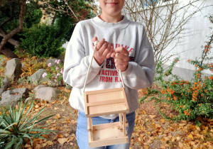 Dziewczynka prezentuje drewniany karmnik.