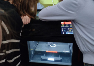 Uczniowie obserwują przebieg wydruku na drukarce 3D.