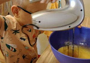 Chłopiec miksuje jajka w misce.