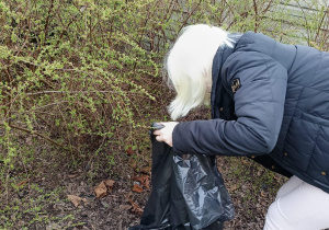 Uczennica zbierająca śmieci do worka.