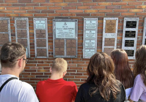 Uczniowie przed tablicą pamiatkową na Cmentarzu Powązkowskim.