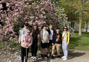Grupa uczniów pozująca na tle kwitnącej na różowo magnolii.