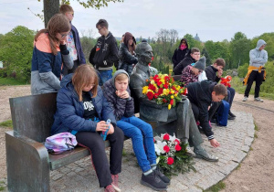 Uczniowie siedzący i stojący wokół pomnika Jana Karskiego.