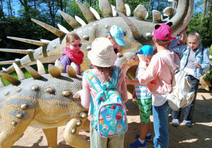 Dzieci dotykają makietę dinozaura.