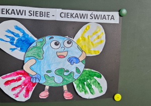 Praca plastyczna - uśmiechnięty świat i cztery dłonie dookoła niego. Nad nimi napis: Ciekawi siebie - Ciekawi świata.