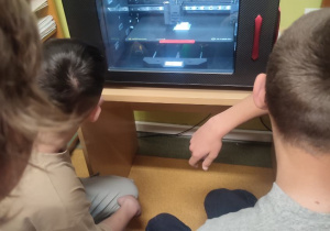 Chłopcy obserwują drukowanie bryły w drukarce 3D.