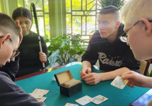Uczniowie przy stole, trzymają karty w rękach.