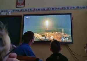 Uczniowie przed monitorem obserwują transmisję ze startu.